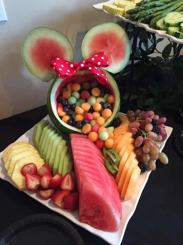 watermelon carved, as minnie mouse, filled with fruit, baby shower themes for girls, sliced fruits, white plate
