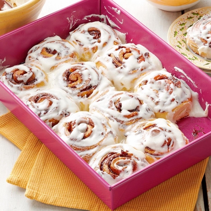 brunch ideas for a crowd, cinnamon buns, with white frosting, in a pink box, yellow cloths