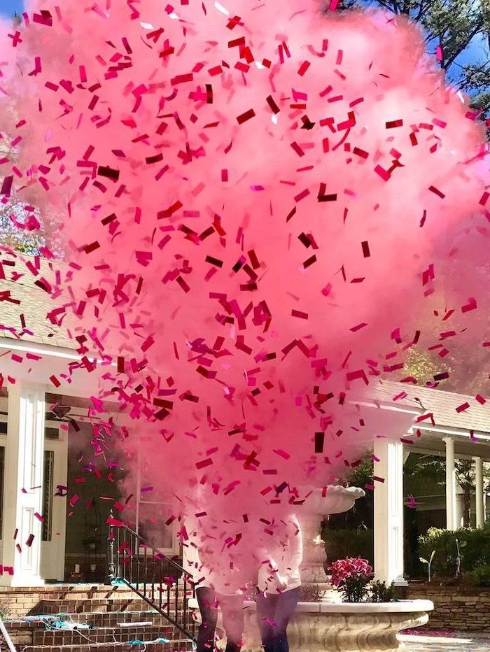 pink smoke, pink confetti, gender reveal games, man and woman standing, in front of a fountain