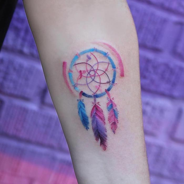 forearm tattoo, watercolor tattoo, pink purple and blue colors, dream catcher tattoo on arm, purple brick wall