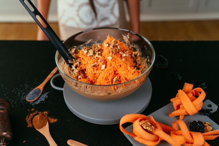 shredded carrots and chopped nuts added to the mix, glass bowl placed on grey board, carrot cake recipe