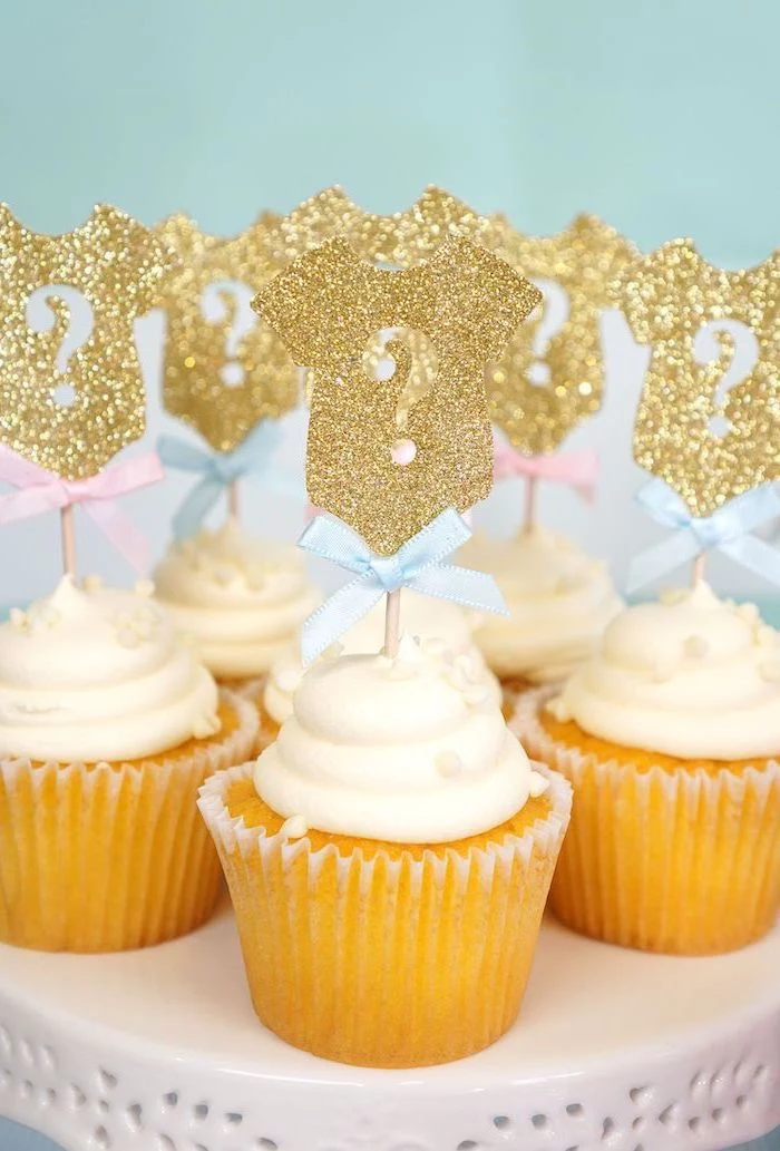 small cupcakes, with white frosting, gold glitter onesies, cake toppers, gender reveal ideas, blue bows