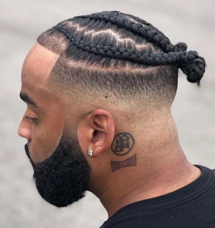 short braids hairstyles, man with black hair, braided in a bun, black beard, black t shirt, neck tattoo