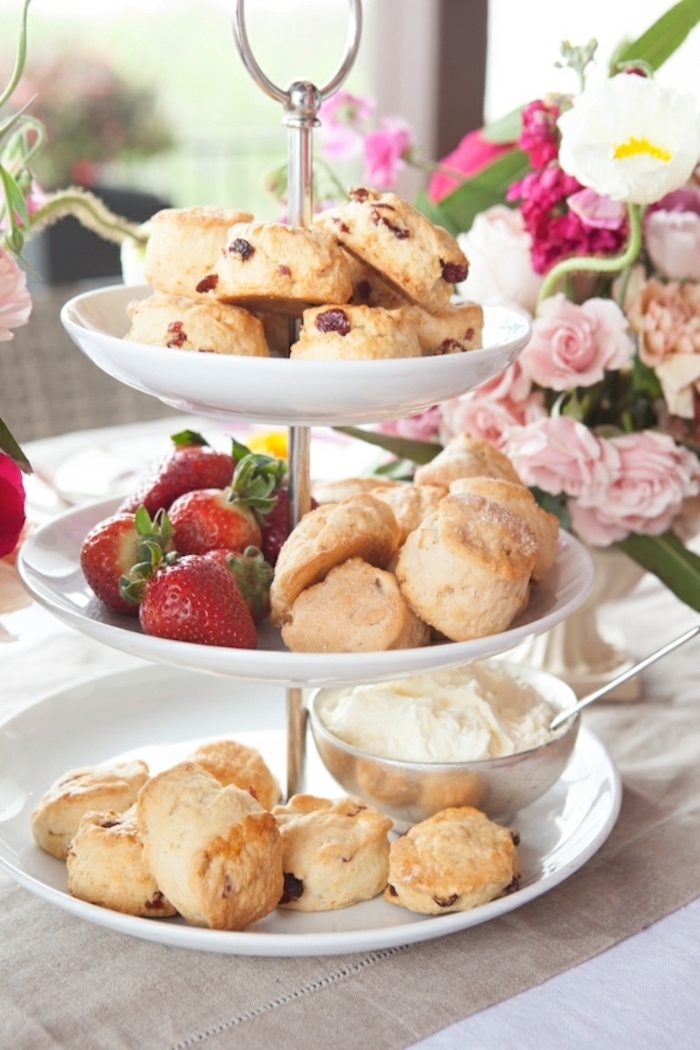 white cake stand, things to make for breakfast, scones and strawberries, cream in a bowl, flower bouquet