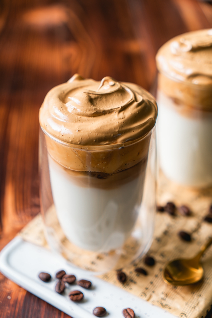 two glass cups, dalgona coffee recipe, filled with milk and ice, whipped coffee on top