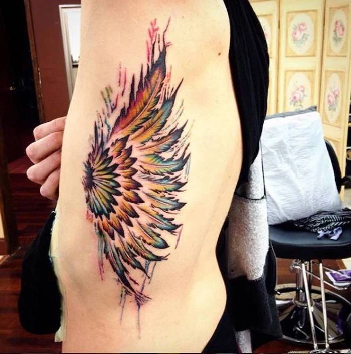 side of the body tattoo, wing tattoo on arm, watercolor tattoo, angel wing, black leather chair in the background