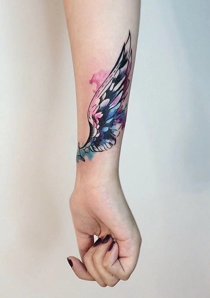 forearm tattoo, watercolor tattoo, wing tattoo on arm, white background, pink and blue colors, black nail polish