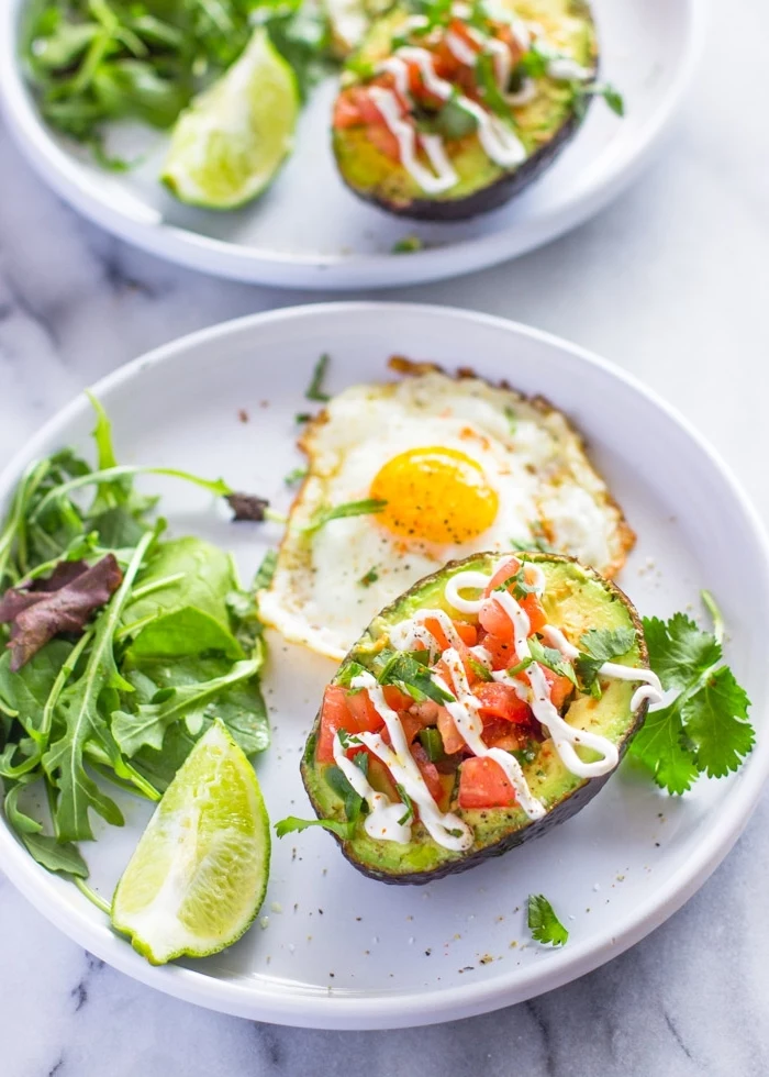 halved avocado, filled with chopped tomatoes, on white plate, fried egg, green salad, breakfast recipes