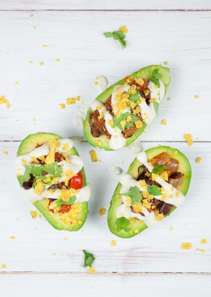 halved avocados, filled with eggs, bacon and tomatoes, sour cream dressing, breakfast finger foods, wooden table