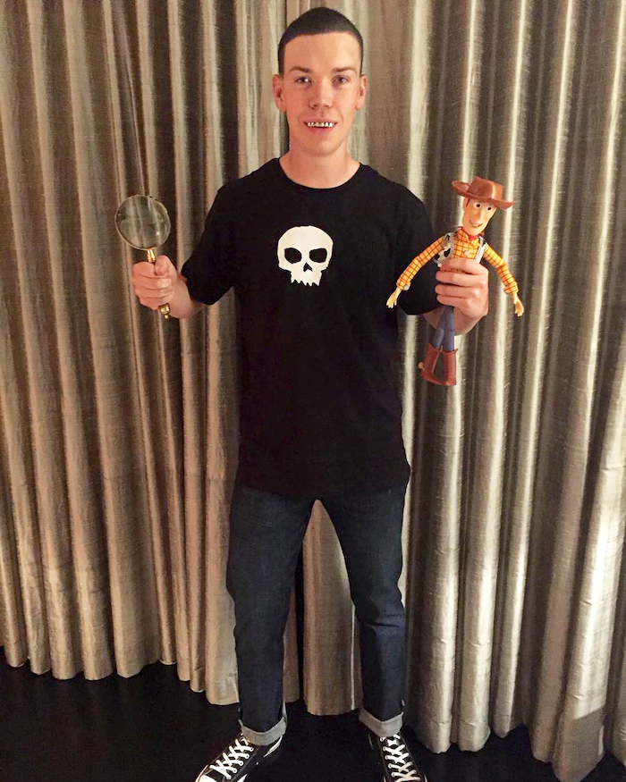 will poulter, dressed as sid, from toy story, halloween costume ideas for men, holding a woody toy, magnifying glass