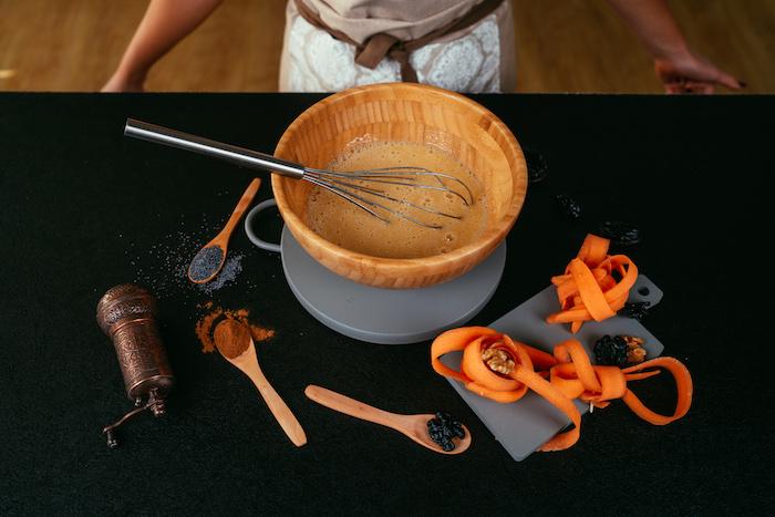 wooden bowls with ingredients whisked inside, carrot cake recipe, placed on grey board on black surface