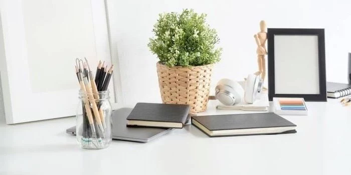 black notebooks, on white desk, potted plant, wooden pot, office cubicle accessories, glass pencil holder