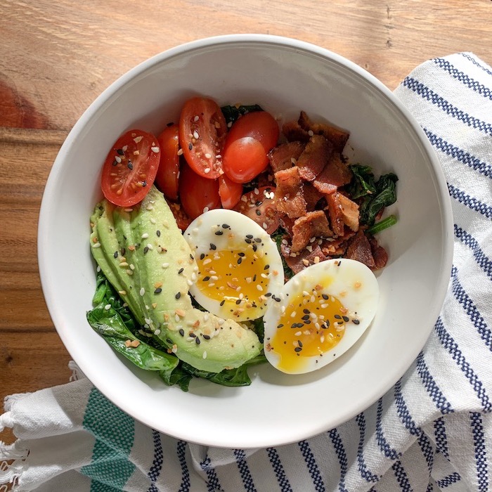 white bowl, easy keto breakfast, boiled egg, cherry tomatoes, avocado slices, bacon inside, wooden table