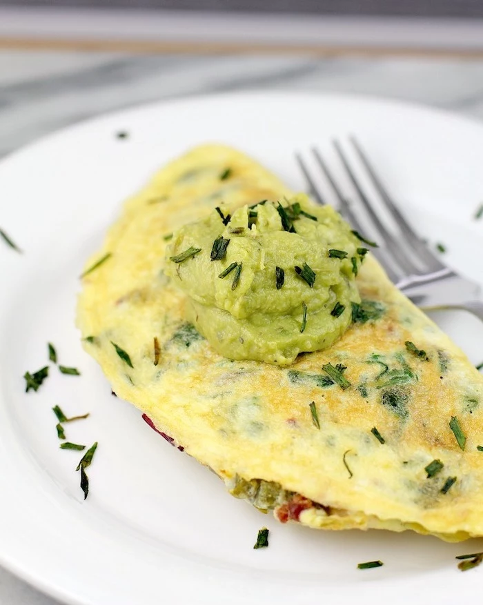 bacon jalapeno omelet, easy keto breakfast, chives and guacamole sauce on top, white plate, silver fork