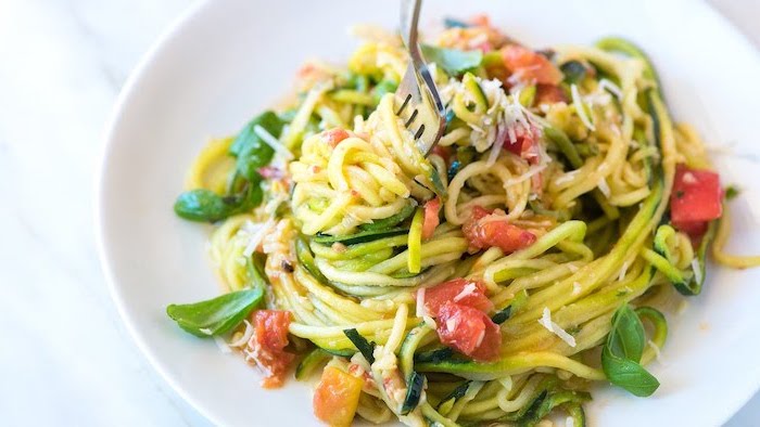 zoozdles with vegetables, cherry tomatoes, grated parmesan on top, white plate, zucchini spaghetti recipe