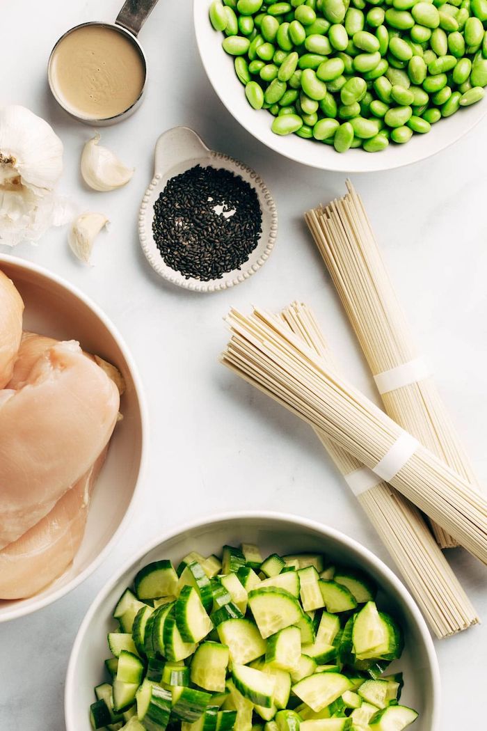 healthy meal prep ideas, beans and cucumbers, chicken fillet, chia seeds, in white bowls, pack of noodles