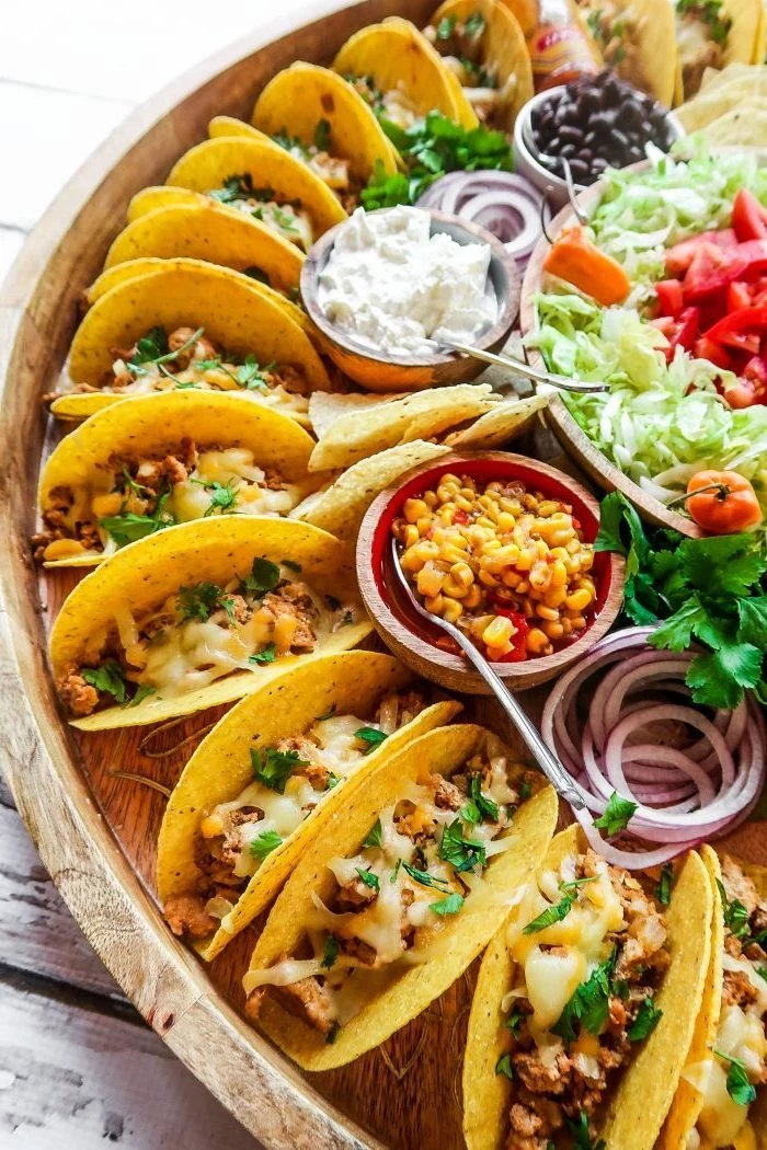 mini tacos, arranged on a large, wooden tray, ground beef taco recipe, glass bowls, different ingredients