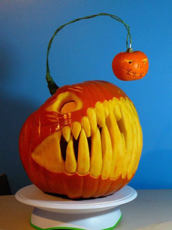 pumpkin with large teeth, carved into it, another smaller pumpkin hanging, funny pumpkin carving, blue wall