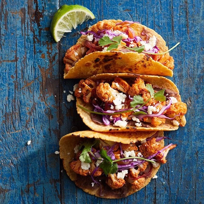 three tacos, with cauliflower, arranged on a blue, wooden table, how to cook taco meat, lime slice