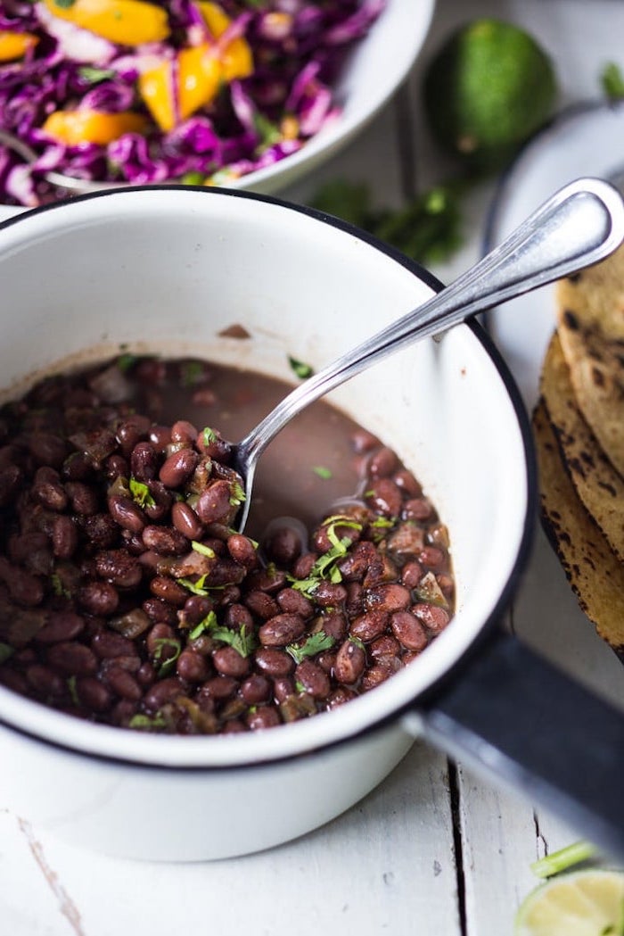 black beans, in a white bowl, white wooden table, taco toppings, chopped cabbage, in a white bowl