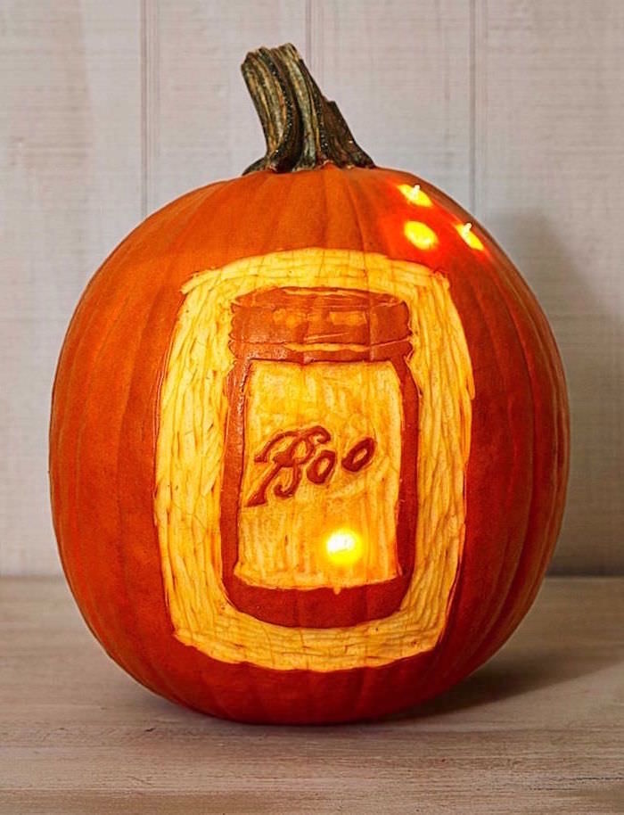 boo mason jar, carved into a pumpkin, lit by candles, wooden background, jack o lantern designs