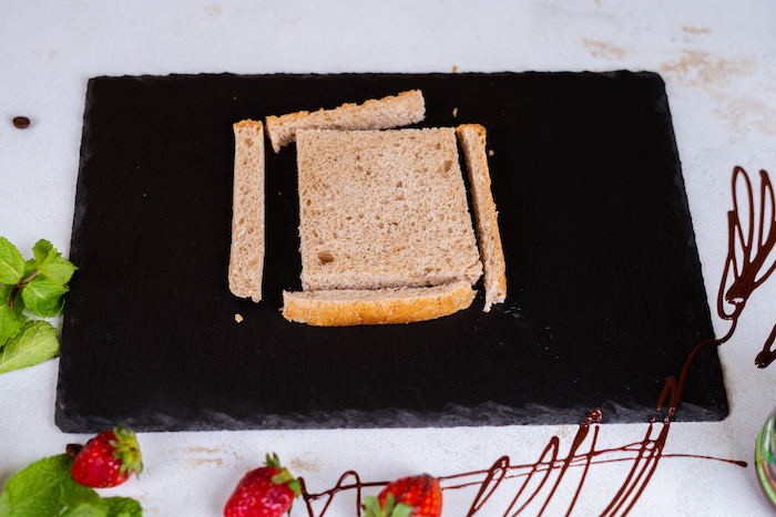 bread slice with the crust cut off, placed on black cutting board, french toast, strawberries and chocolate around it