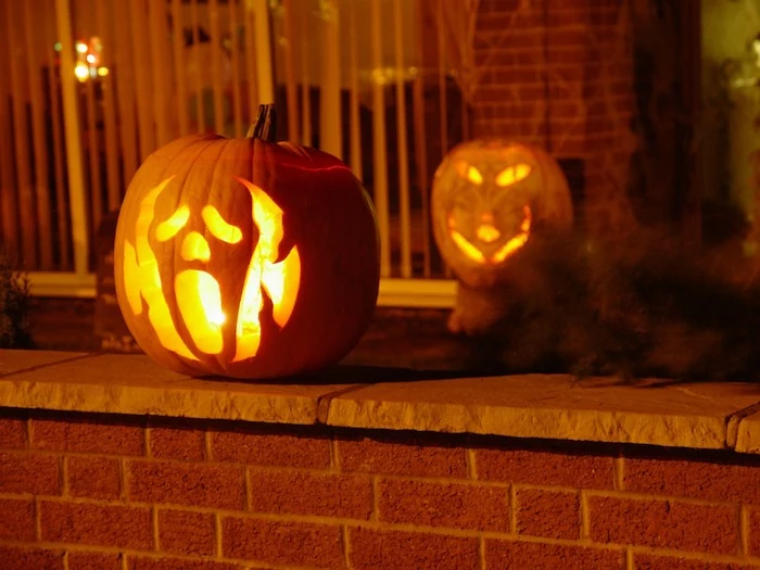 two pumpkins, ghost face carved into one, cat face carved into the other, pumpkin carving ideas, brick wall