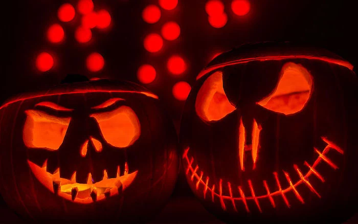 two pumpkins, lit by candles, scary faces, carved on them, black background, pumpkin carving ideas