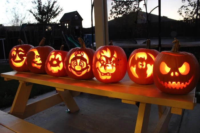 different pumpkins, different faces carved on them, on a wooden table, pumpkin carving ideas, lit by candles
