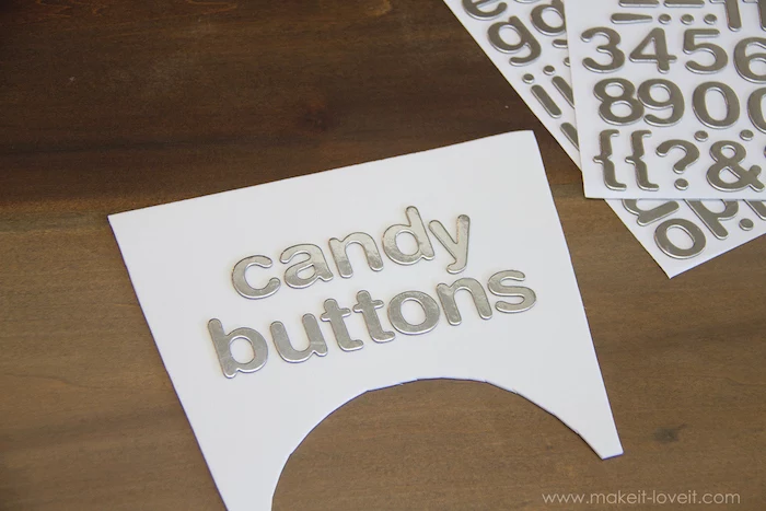 silver letters, candy buttons, glued to white paper, baby costumes for boys, wooden table