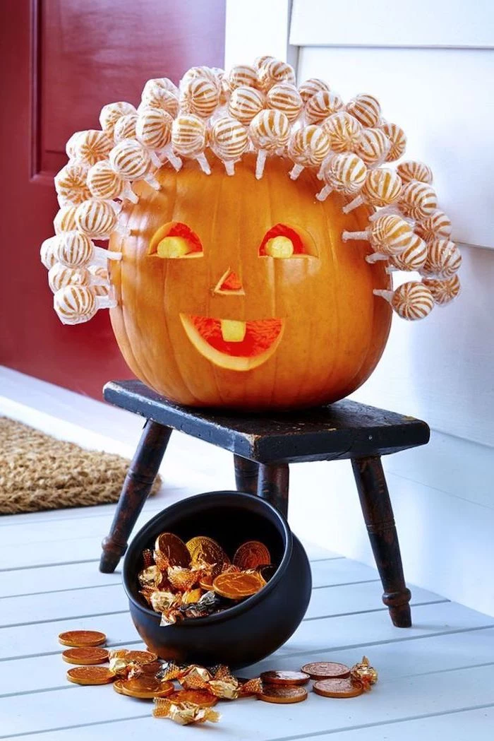 lollipops stuck onto a pumpkin, on a black wooden stool, jack o lantern designs, candies scattered around