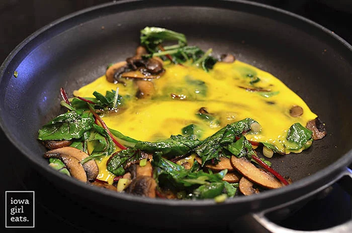 spinach and eggs, mushrooms in a black, frying pan, best keto recipes, black background