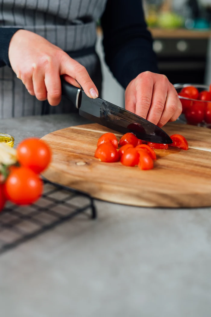cherry tomatoes being halved with black knife on wooden cutting board how to make zoodles
