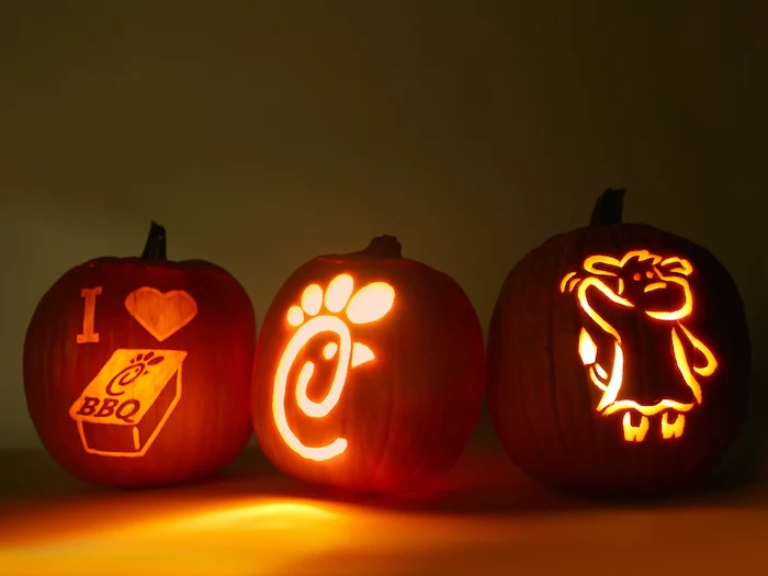 chick fil a inspired, three pumpkins, lit by candles, jack o lantern designs, dark background