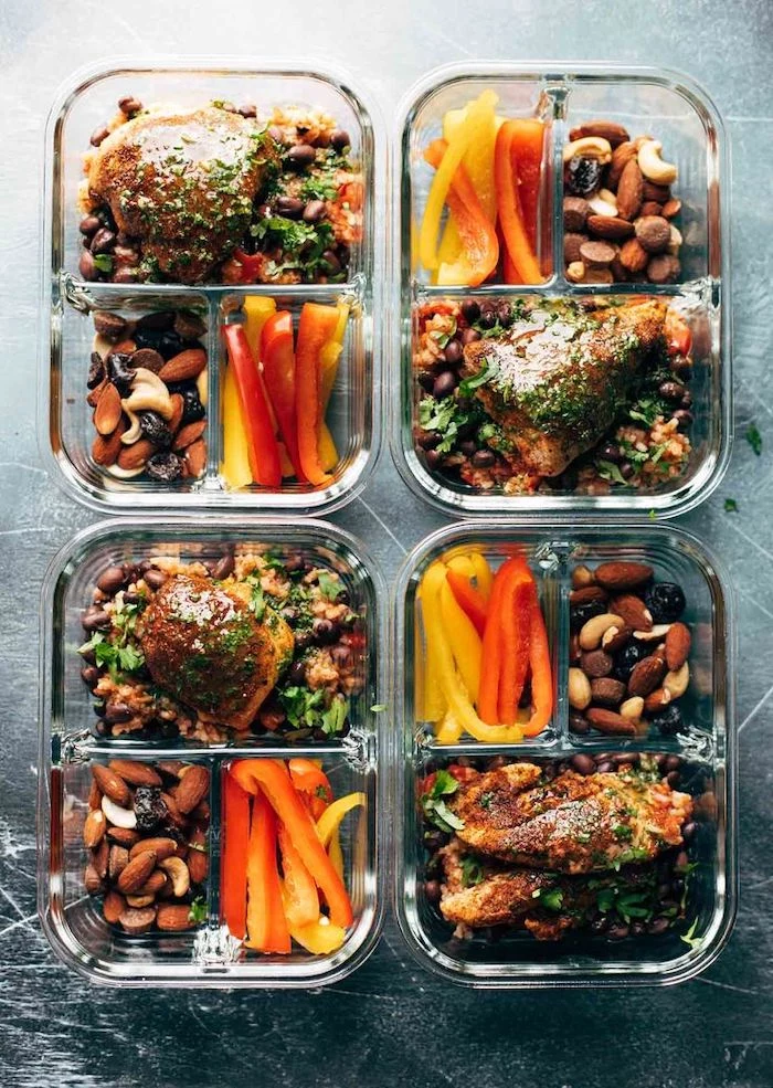 four glass containers, chicken fillet, peppers and nuts on the side, black wooden table, healthy meal prep ideas
