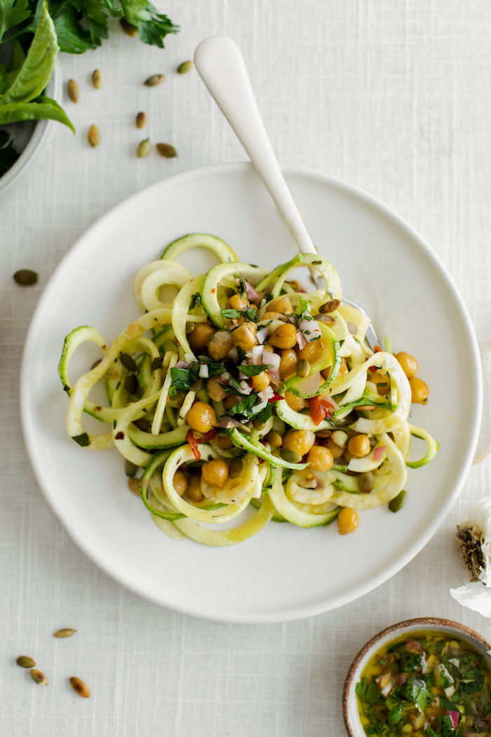 zoodles with chickpeas, in a white plate, white spoon, white table, how to cook spiralized zucchini noodles