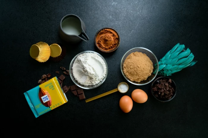 cocoa and flour, eggs and milk, different ingredients, arranged on black countertop, chocolate cupcakes