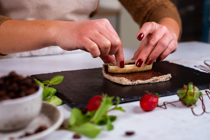 bread slice with chocolate and banana inside, rolled up, placed on black cutting board, french toast