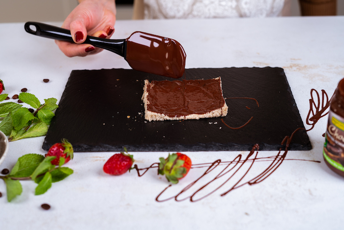 bread slice with the crust cut off, chocolate spread on it with black spatula, french toast, placed on black cutting board