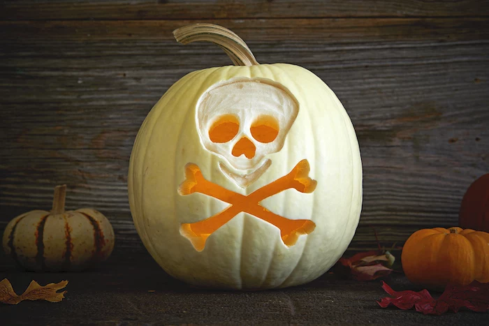 white pumpkin, skull carved into it, pumpkin carving ideas, wooden background, lit by candles