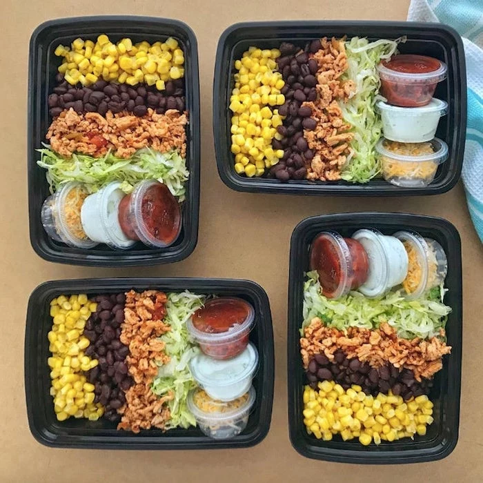 four black, plastic containers, easy healthy lunch ideas, corn and meat, black beans, green salad, sauces and cheese