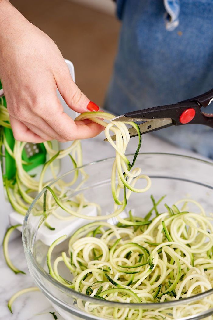 cutting zucchini noodles, with scissors, how to make zoodles, in a glass bowl, red nail polish