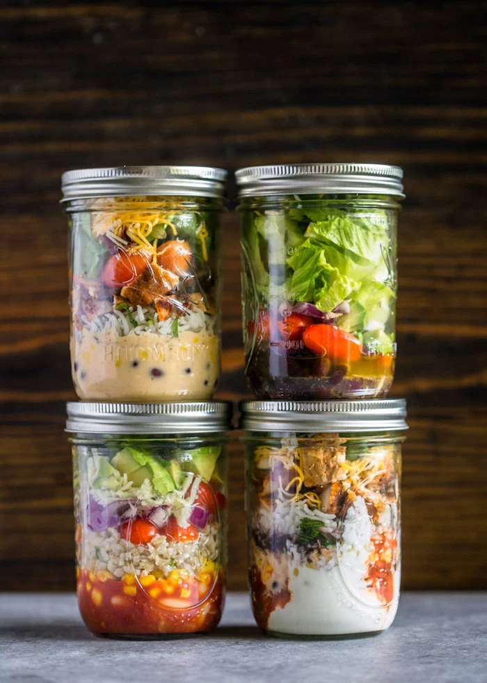 four mason jars, filled with different salads, easy healthy lunch ideas, wooden background, granite countertop