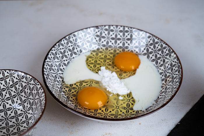 french toast recipe, two eggs and sugar mixed together in a black and white ceramic bowl, placed on white countertop