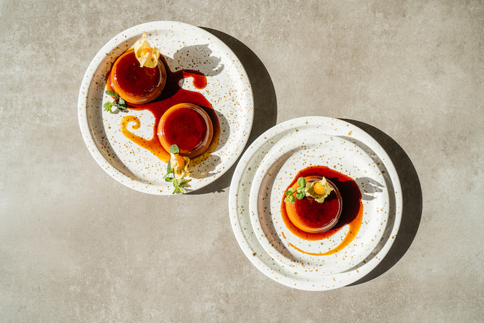 creme caramel recipe, three flans placed on white plates, decorated with flowers and mint leaves, placed on grey surface