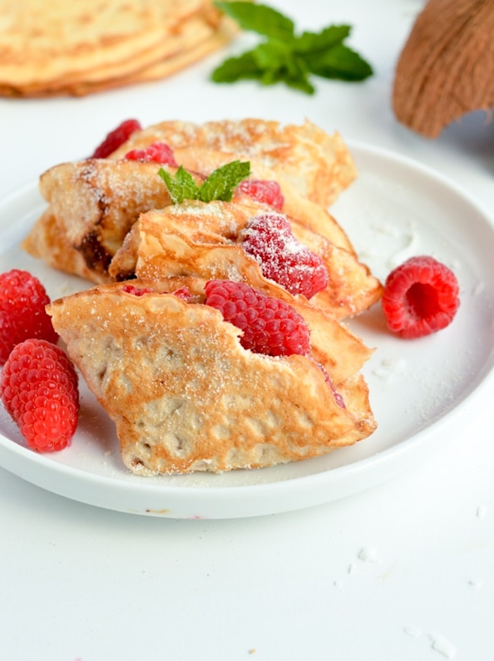 folded crepes, raspberries inside, keto diet recipes, raspberries in white plate, coconut flakes, powdered sugar