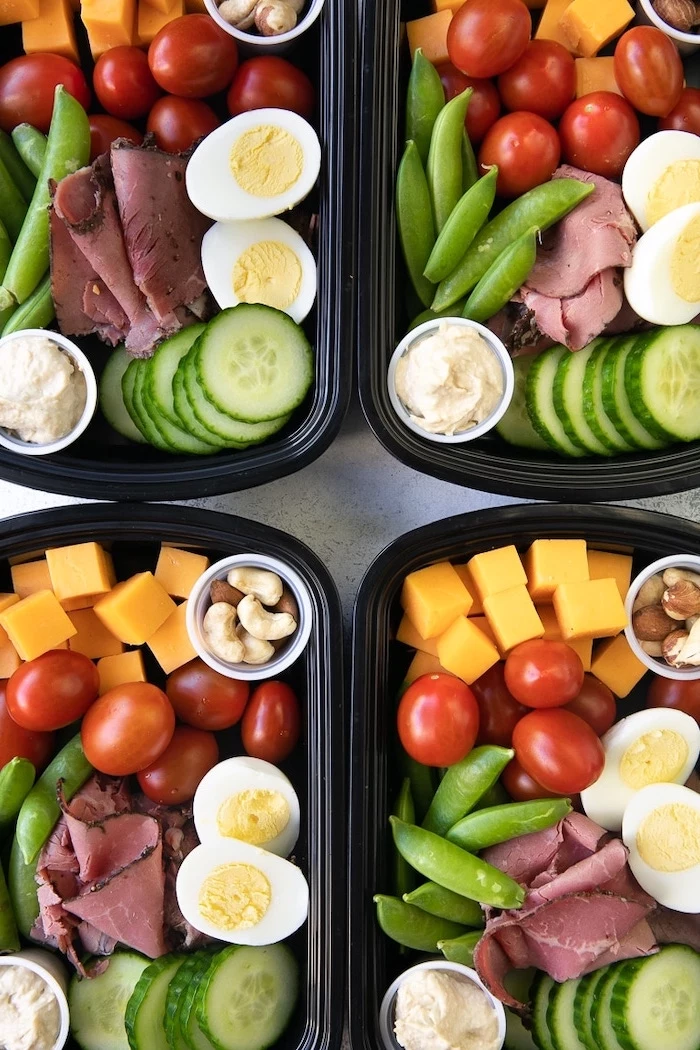 four black, plastic containers, healthy lunches for work, ham and cucumbers, cherry tomatoes, cheese and nuts inside