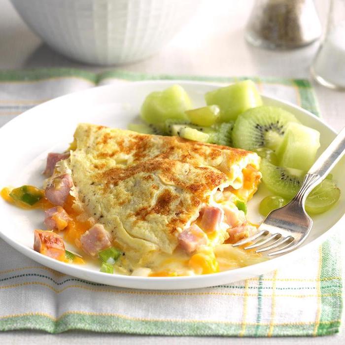 egg omelet, with ham and cheese, low carb breakfast recipes, kiwi and grape slices, on the side, white plate