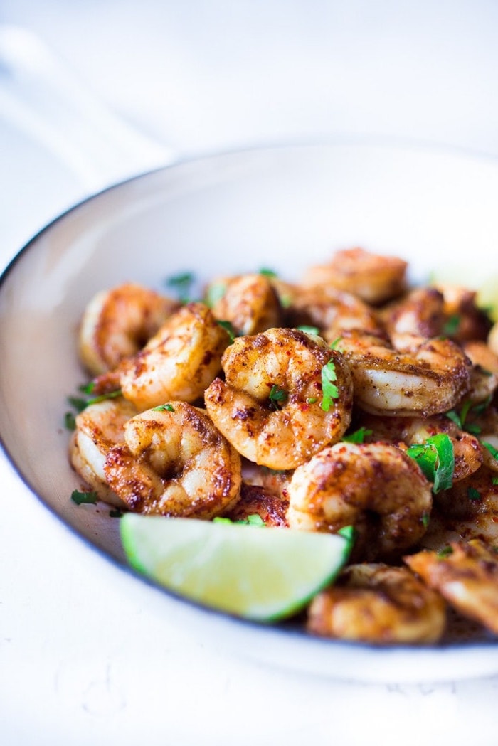 white bowl, filled with fried shrimp, lime slice on top, taco toppings, white table