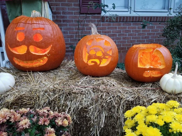 three pumpkins, arranged on a haystack, flowers around, brick wall, pumpkin faces ideas